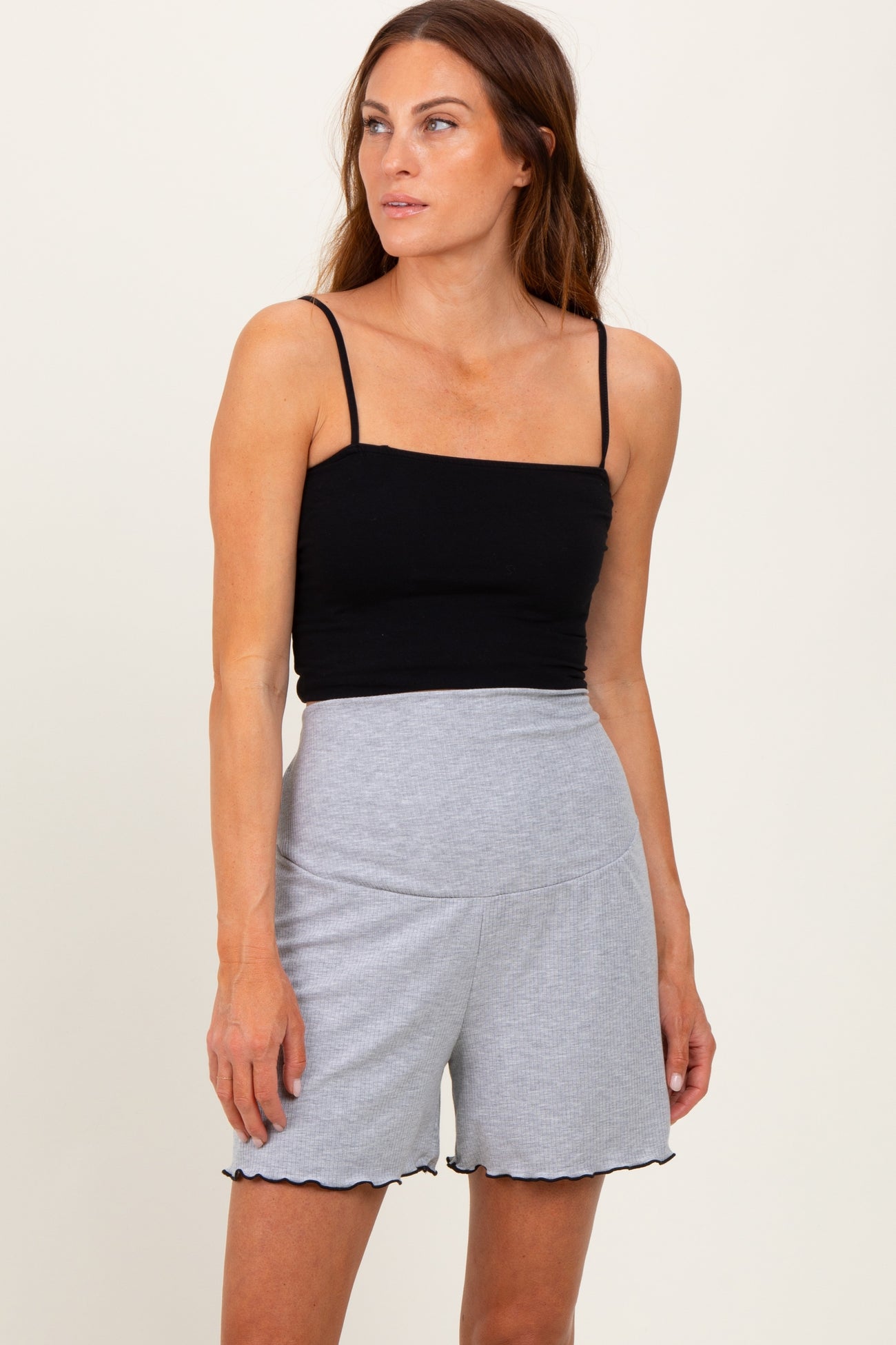 woman wearing a black fitted tank top and gray high-waisted shorts with scalloped edges