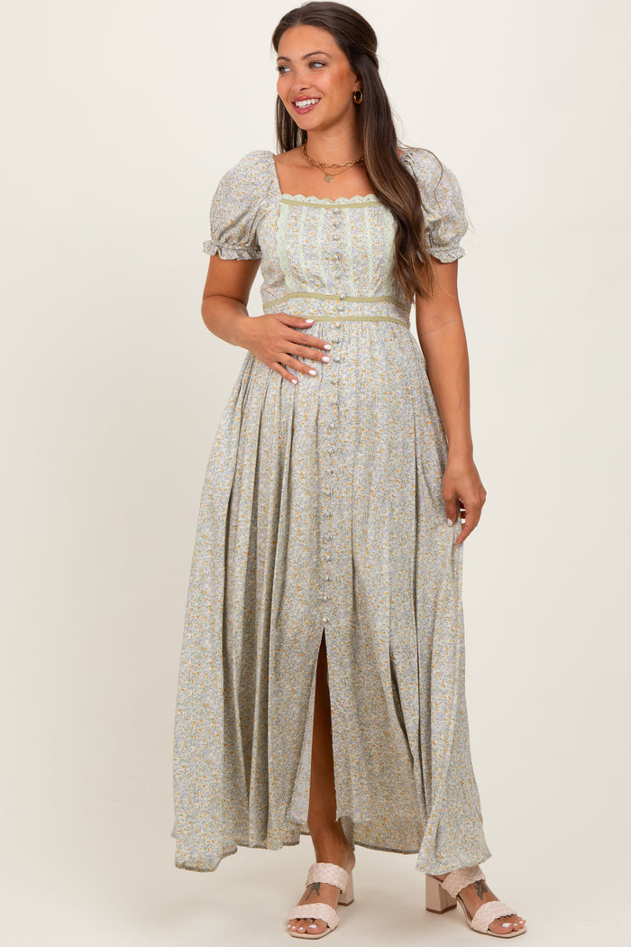 woman wearing a light green floral maternity maxi dress with puff sleeves and a front slit, holding her baby bump