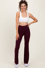 woman wearing a white crop top and burgundy flared workout leggings, smiling and posing with one hand on her hip