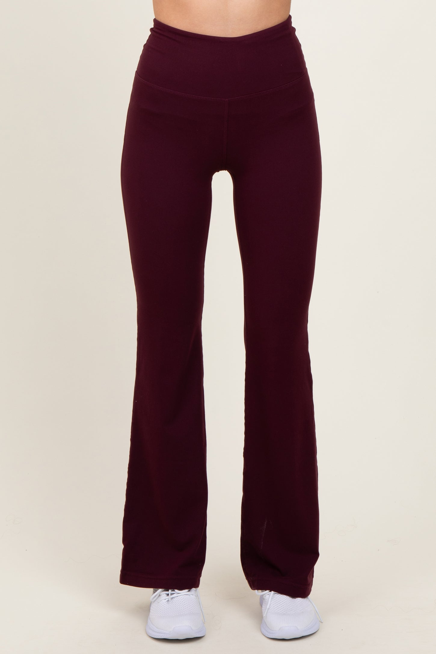 woman wearing burgundy flared workout leggings with a high waistband and paired with white athletic shoes