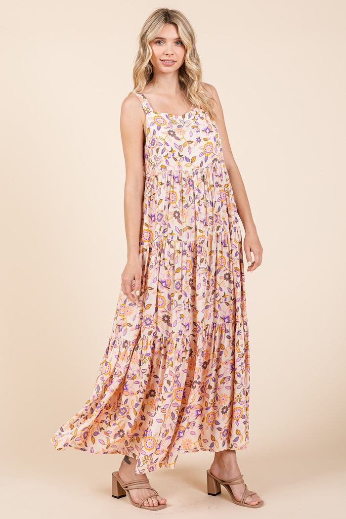 woman wearing a floral pink maxi dress with thin straps and a tiered design in a light, flowy fabric