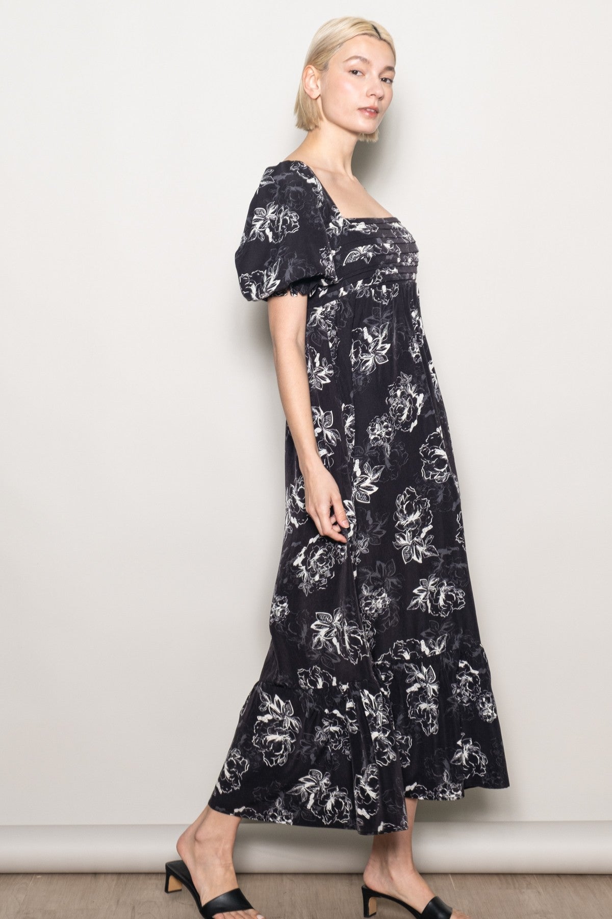 woman wearing a black maxi dress with floral print and puff sleeves, standing against a neutral background