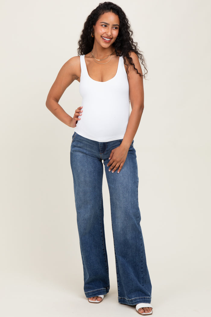 woman wearing a white maternity tank top and blue flared maternity jeans, showing her baby bump