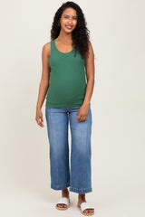 woman wearing a green ribbed maternity tank top and blue wide-leg jeans, showing her baby bump