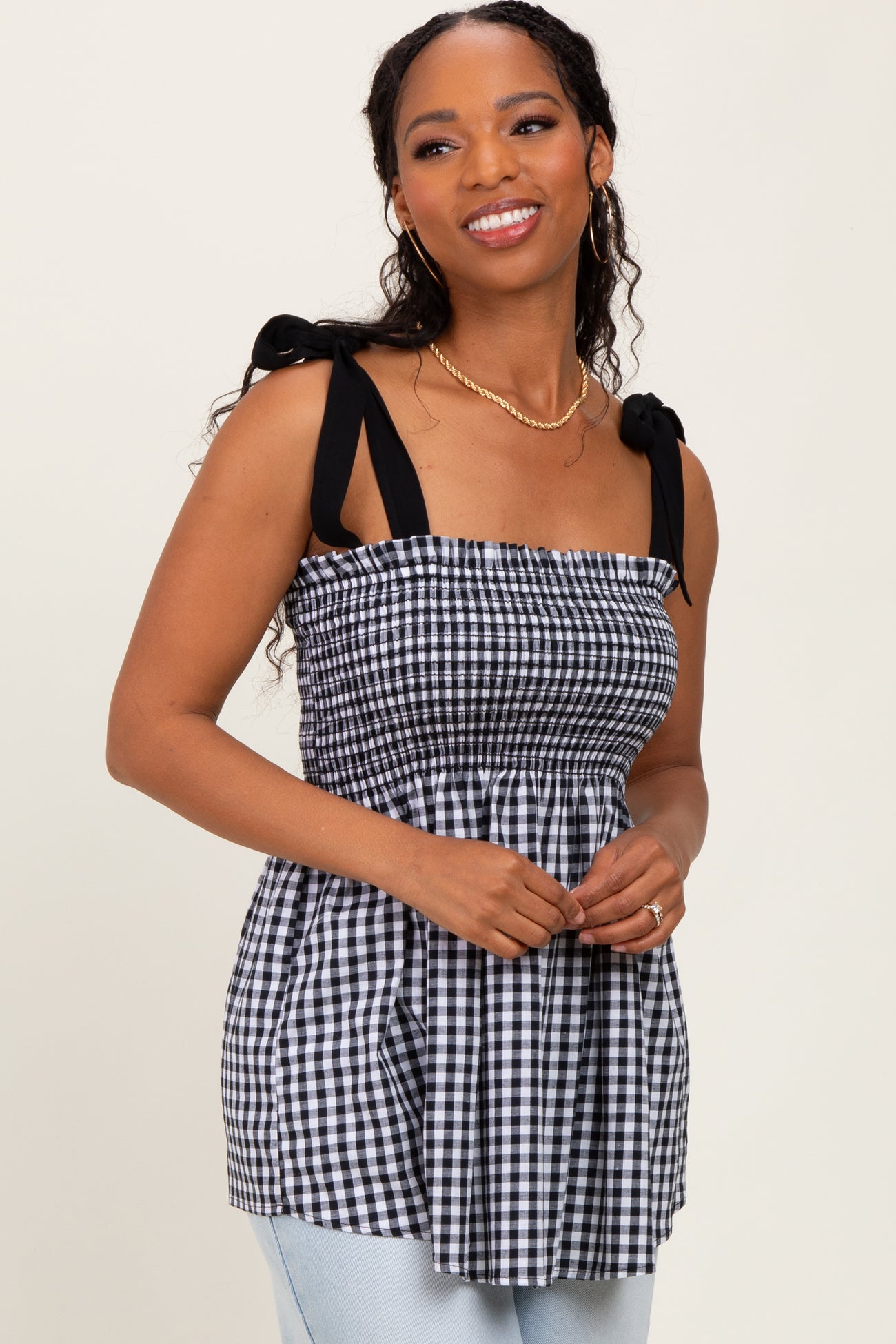 woman wearing a black and white gingham smocked top with tied shoulder straps and a peplum silhouette