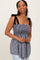 woman wearing a black and white gingham smocked top with tied shoulder straps and a peplum silhouette
