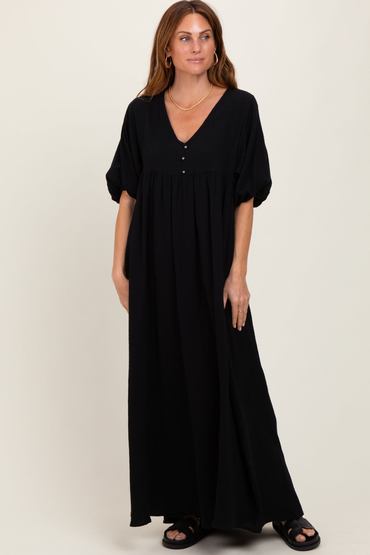 woman wearing a black maxi dress with a v-neckline, short puff sleeves, and button details, standing on a neutral background