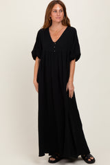 woman wearing a black maxi dress with a v-neckline, short puff sleeves, and button details, standing on a neutral background