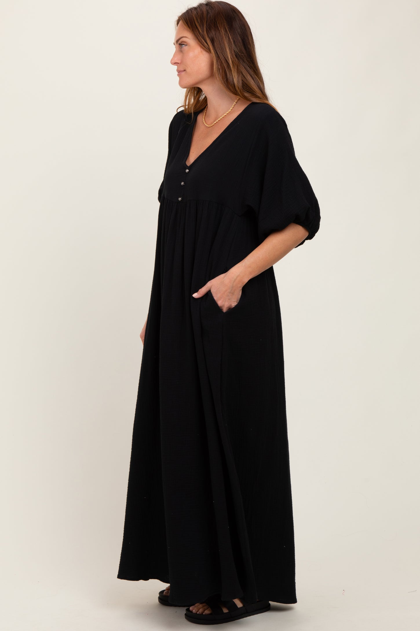woman wearing a black maxi dress with a v-neck, buttons, puff sleeves, and side pockets