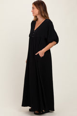woman wearing a black maxi dress with a v-neck, buttons, puff sleeves, and side pockets
