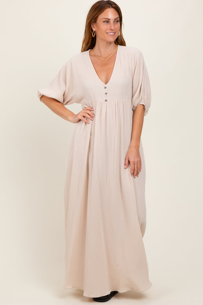 woman wearing a light beige maxi dress with a deep v-neck and button details, standing with hands on hips