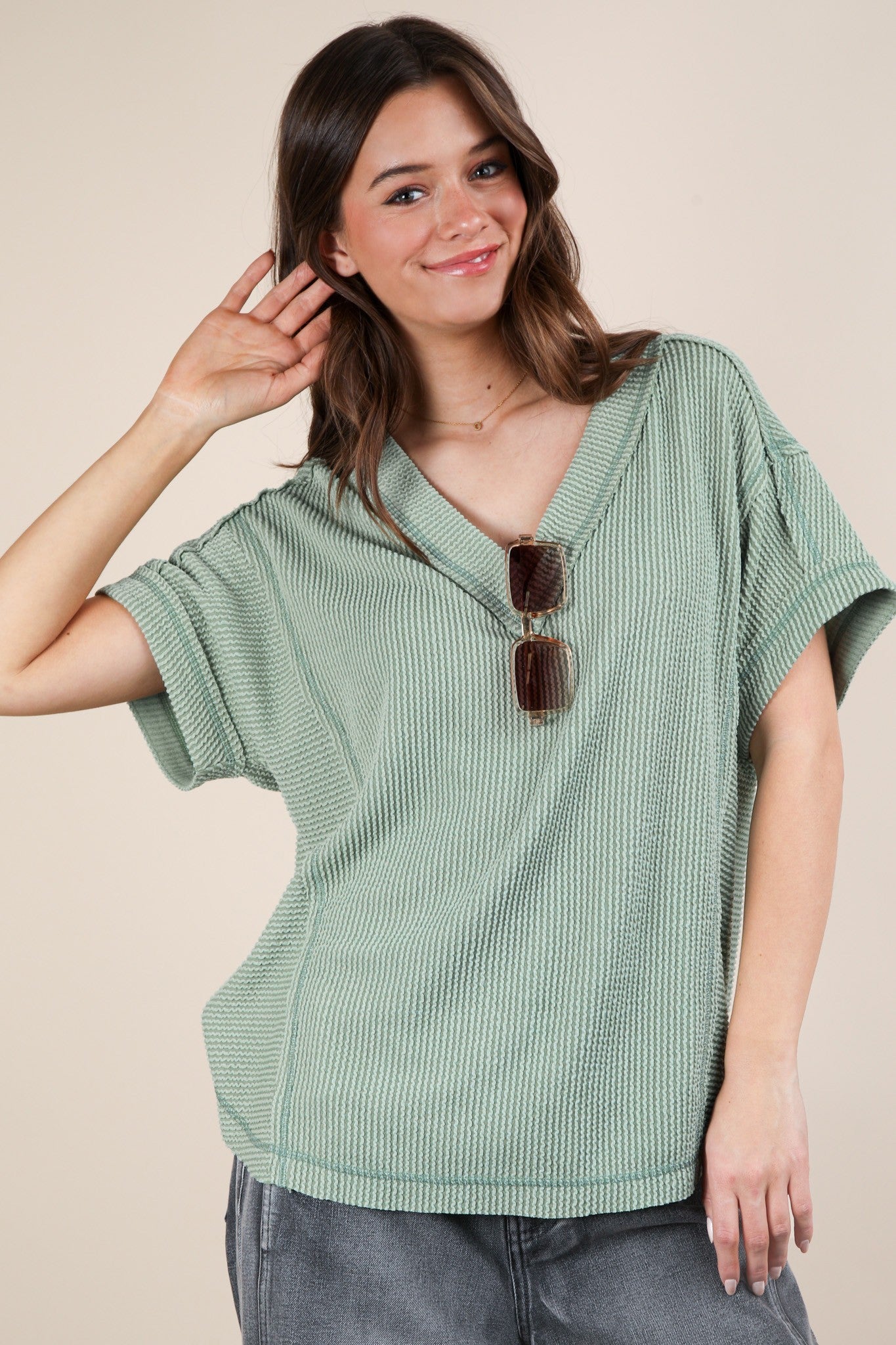 woman wearing a mint green loose-fitting v-neck top with short sleeves and holding sunglasses