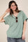 woman wearing a mint green loose-fitting v-neck top with short sleeves and holding sunglasses
