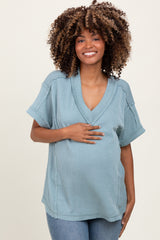 woman wearing a light blue short sleeve maternity sweater and holding her baby bump