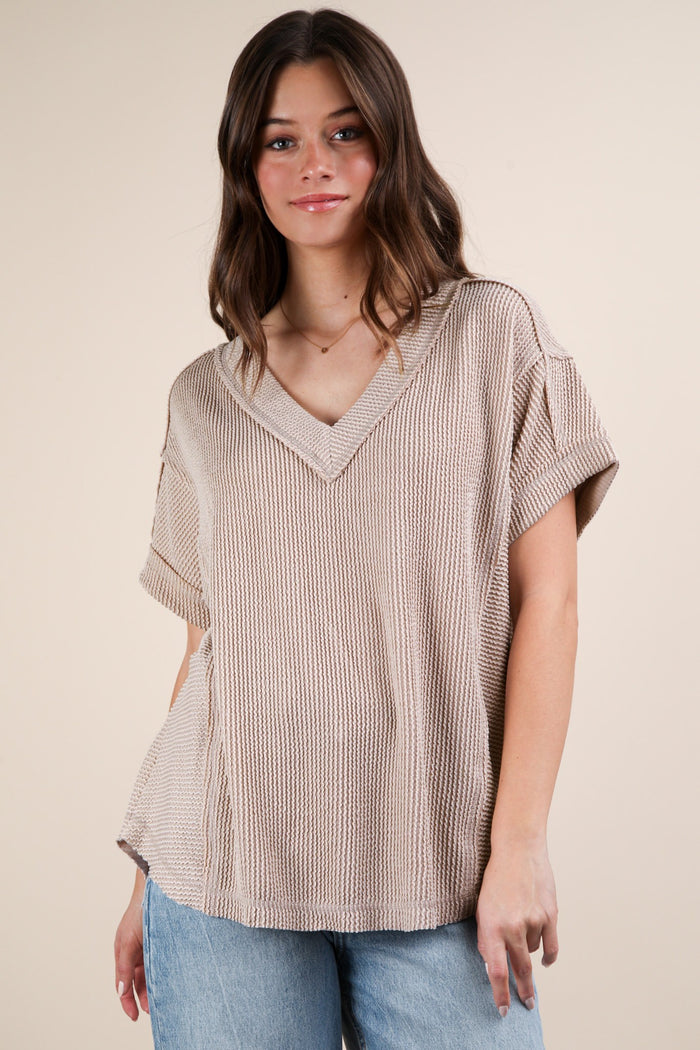 woman wearing a beige oversized v-neck knit top with short sleeves and a relaxed fit
