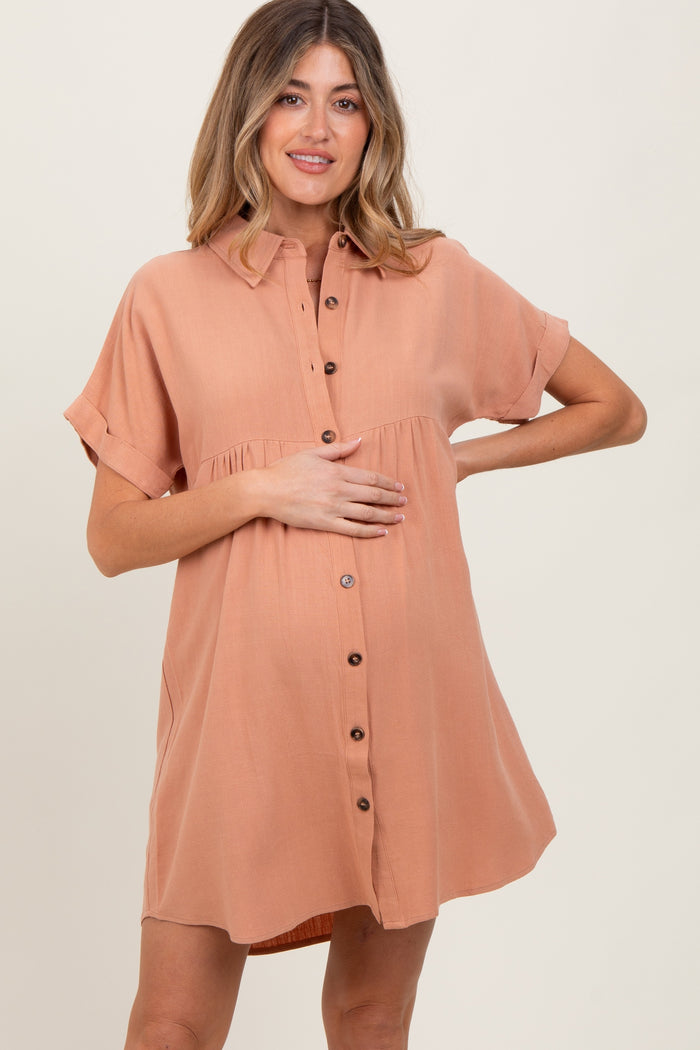 woman wearing a rust-colored maternity button-up dress with short sleeves and a gathered waist, holding her baby bump