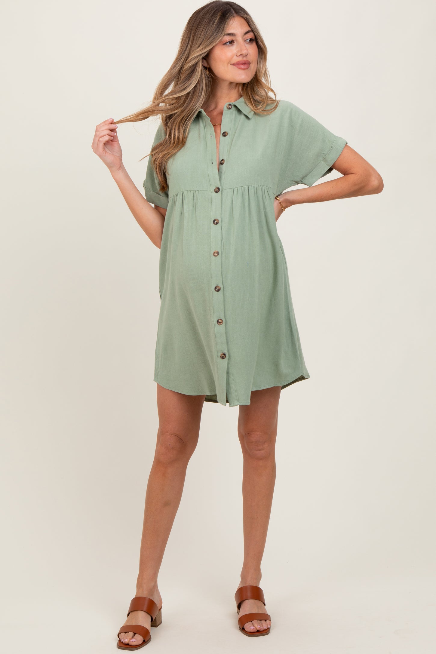 woman wearing a sage green short sleeve maternity dress with buttons and a gathered waist, showing her baby bump
