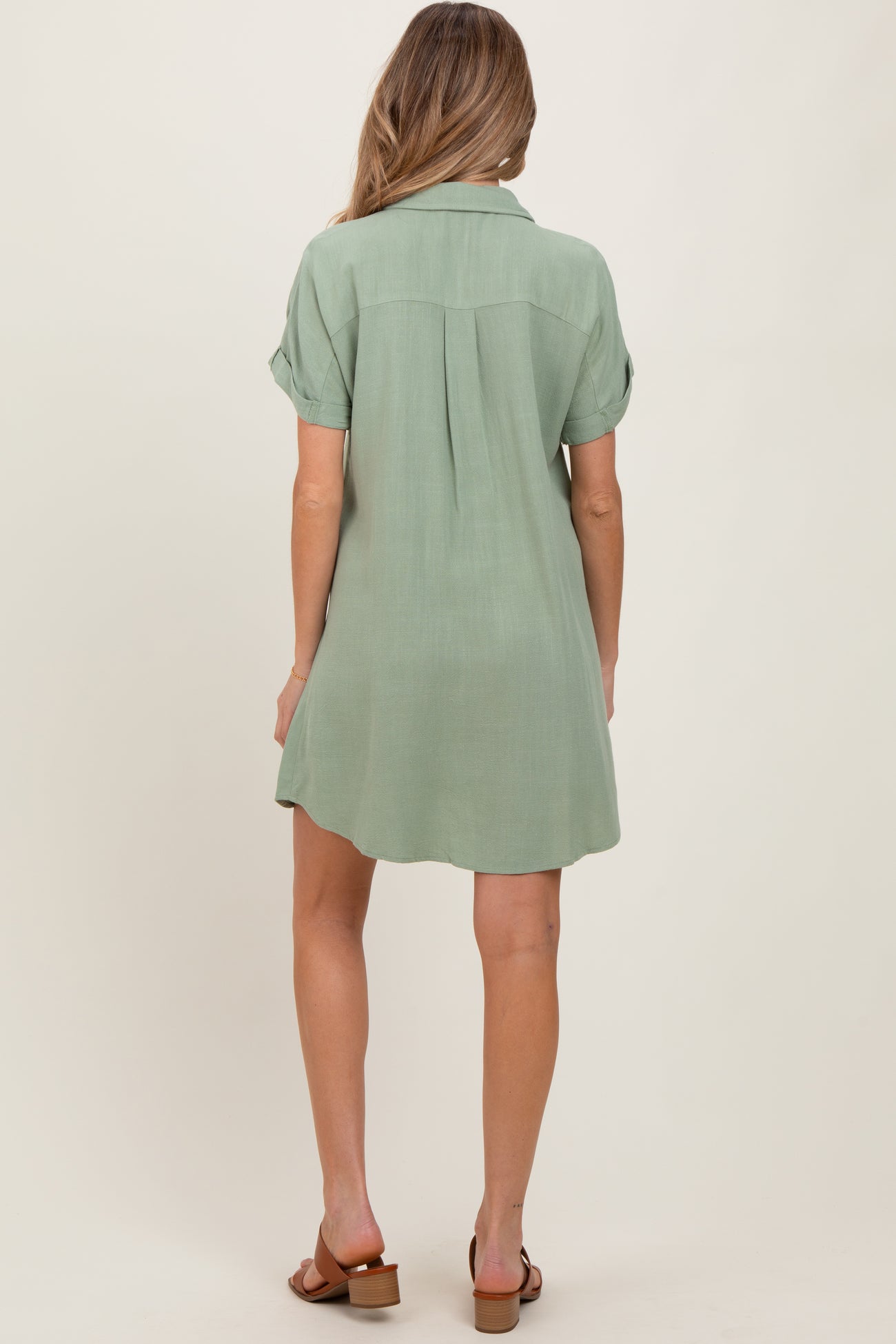 woman wearing a sage green short sleeve maternity dress with a relaxed fit and back pleat detail