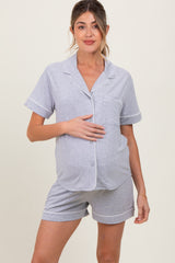 woman wearing a gray short sleeve maternity pajama set with white piping and holding her baby bump