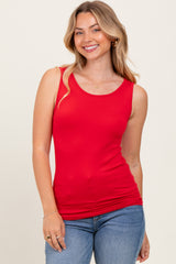 woman wearing a red sleeveless top paired with blue jeans, smiling at the camera