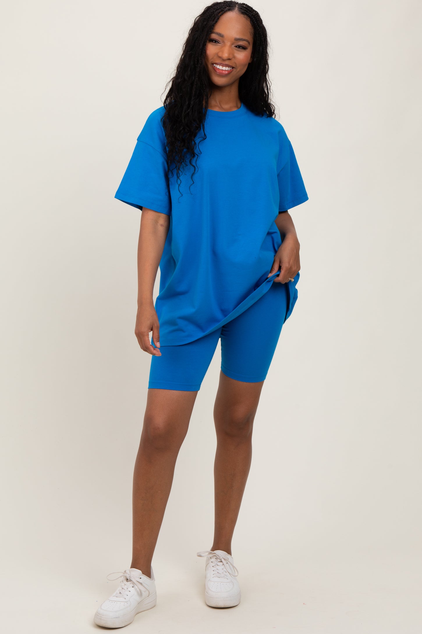 woman wearing an oversized bright blue t-shirt and matching bike shorts, standing and smiling