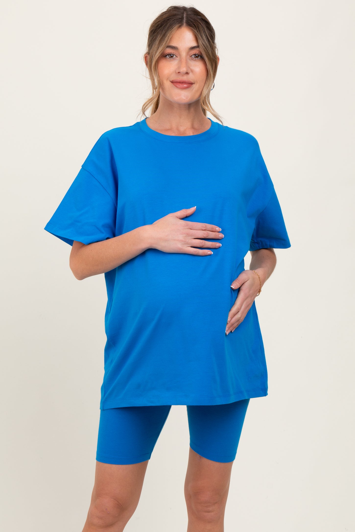 woman wearing a bright blue maternity t-shirt and shorts, holding her baby bump