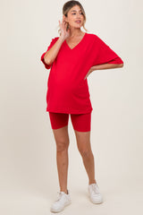 woman wearing a bright red maternity t-shirt and matching biker shorts, showcasing her baby bump