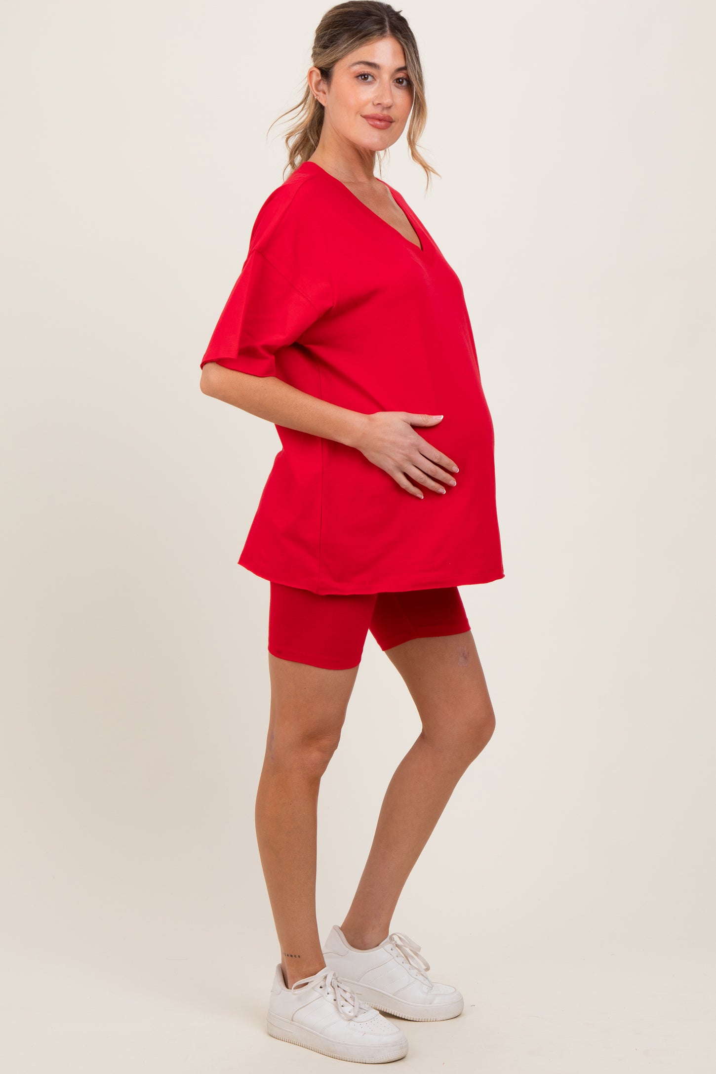 woman wearing a red v-neck maternity top and coordinating red shorts, holding her baby bump