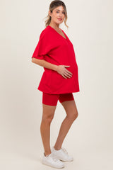 woman wearing a red v-neck maternity top and coordinating red shorts, holding her baby bump