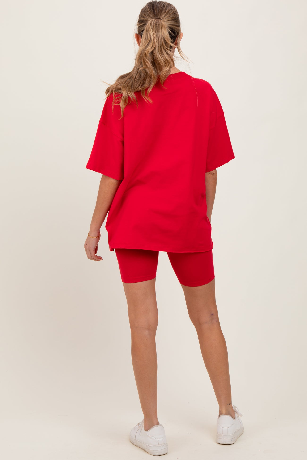 woman wearing a red oversized t-shirt and matching red bike shorts, showing a casual maternity outfit from the back