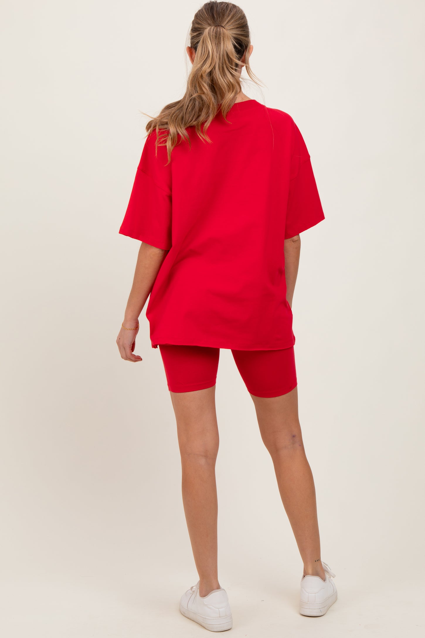 woman wearing a red oversized t-shirt and matching red bike shorts, showing a casual maternity outfit from the back