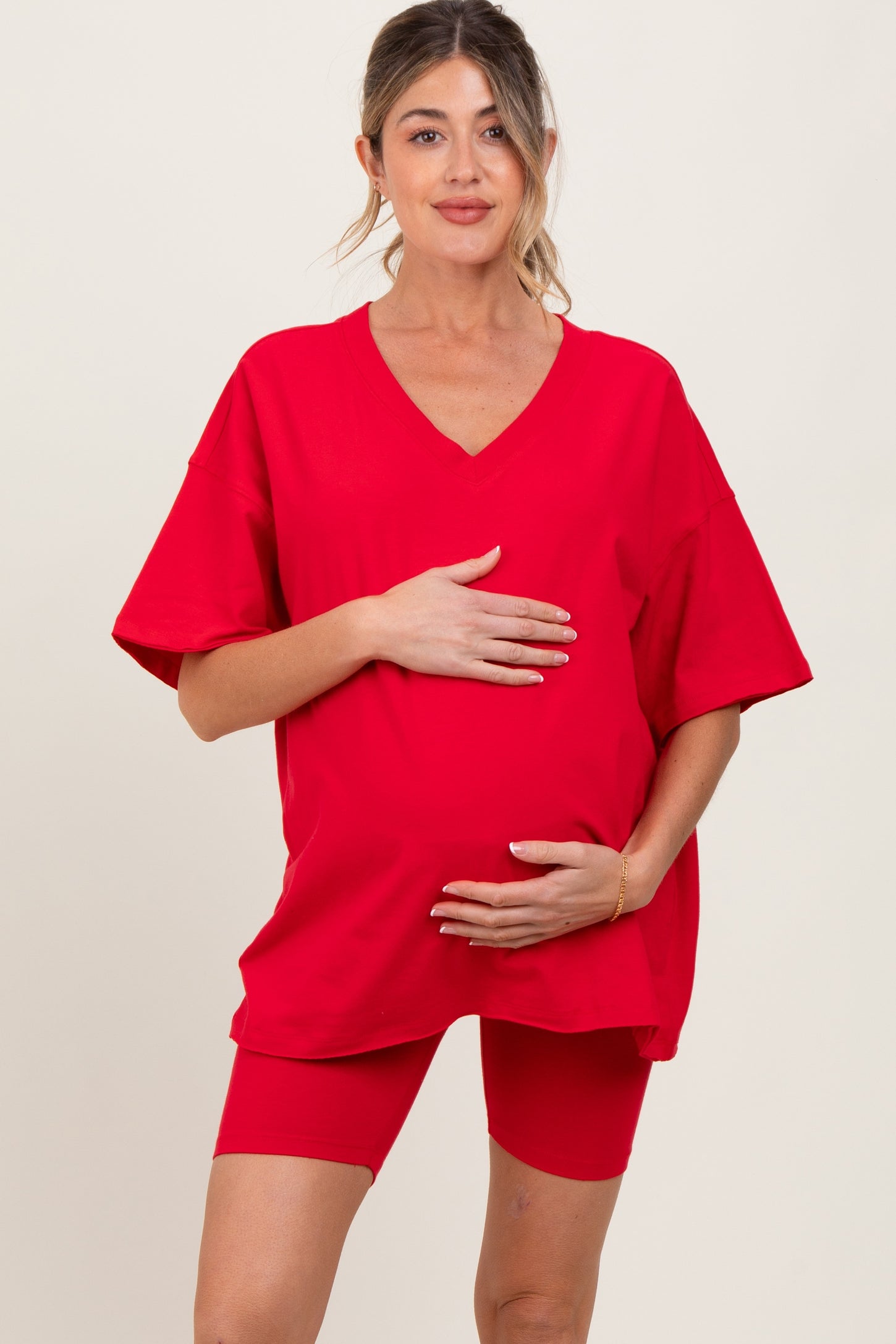 woman wearing a red oversized maternity t-shirt and red maternity bike shorts, holding her baby bump