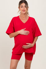 woman wearing a red oversized maternity t-shirt and red maternity bike shorts, holding her baby bump