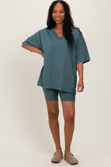 woman wearing a teal oversized v-neck t-shirt and matching bike shorts, standing with hands on hips