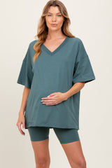 woman wearing a teal maternity oversized v-neck top and matching bike shorts, gently cradling her baby bump