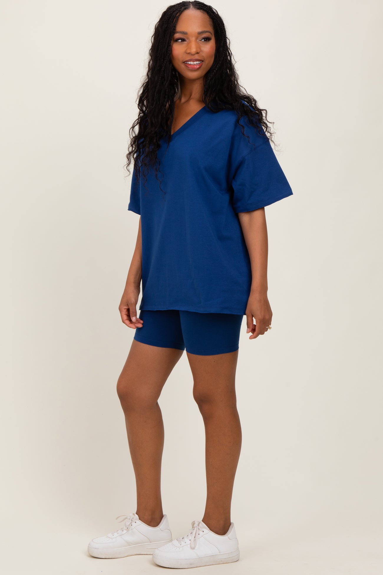 woman wearing a navy blue oversized v-neck t-shirt and matching bike shorts, standing in white sneakers