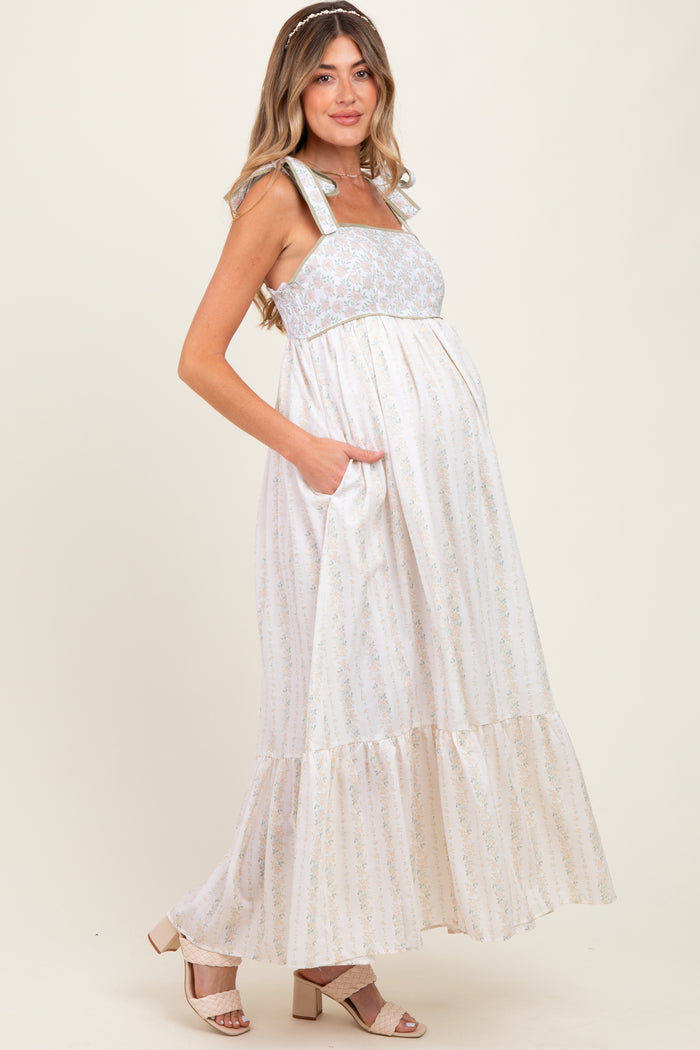 woman wearing a cream floral print maternity maxi dress with pockets and a ruffled hem, showcasing her baby bump