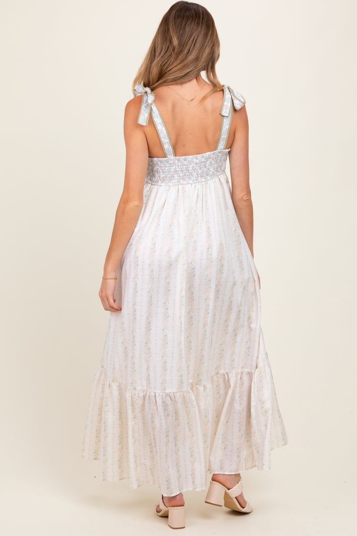 woman wearing a cream and blue floral print maternity maxi dress with tie straps and a smocked back