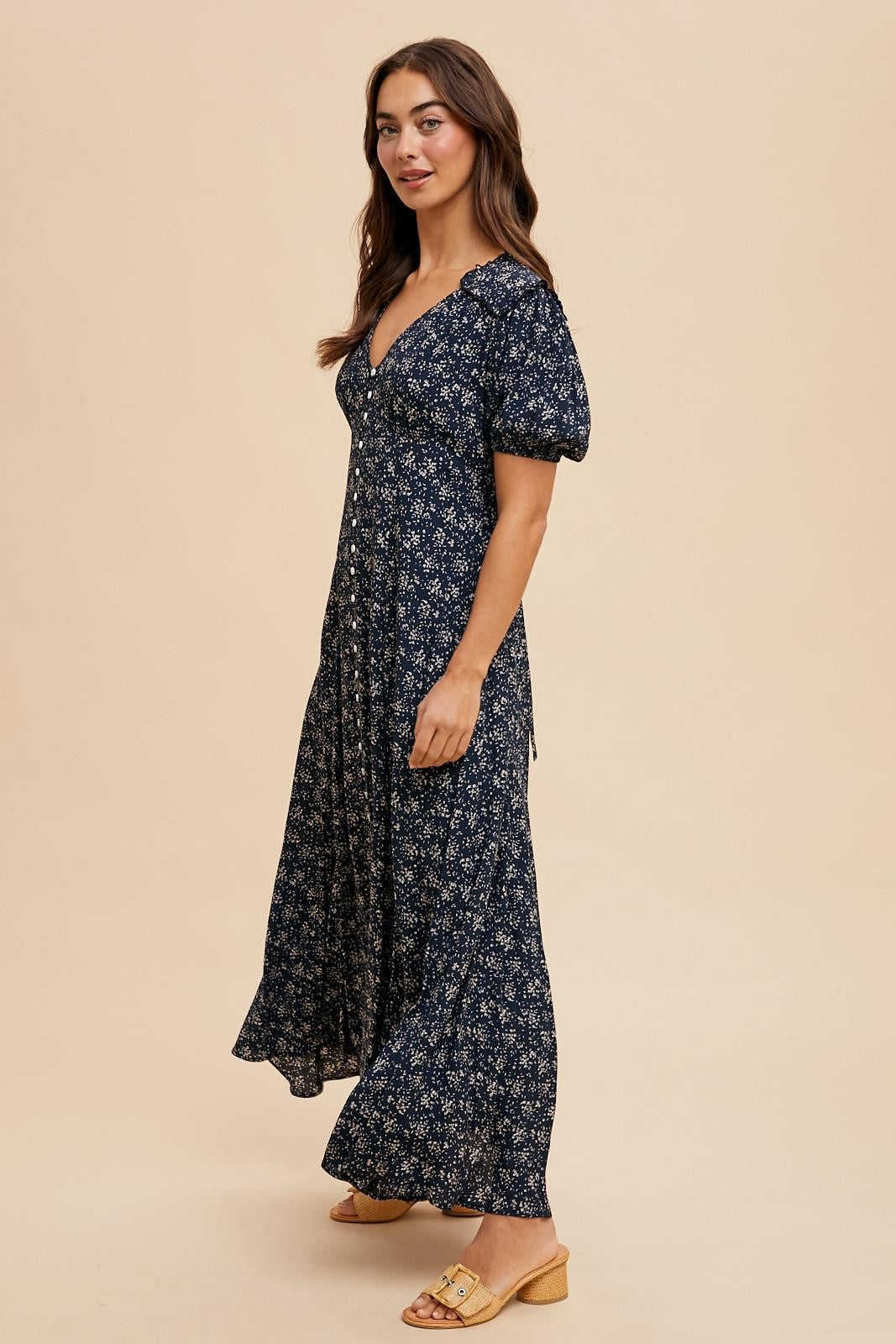 woman wearing a navy floral maxi dress with puff sleeves and a v-neckline, posing against a beige background