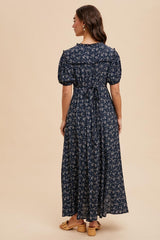 woman wearing a navy blue maxi dress with short puff sleeves and a floral print, view from the back