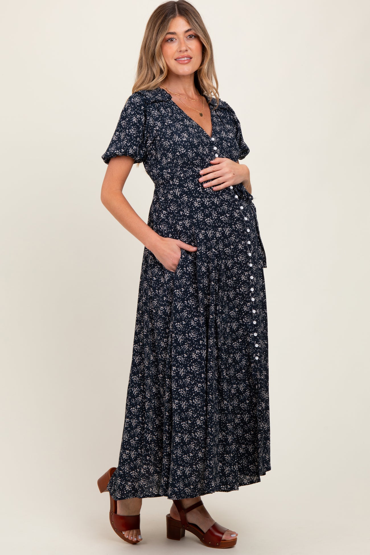 woman wearing a navy blue floral maternity maxi dress with short sleeves and pockets, showcasing her baby bump