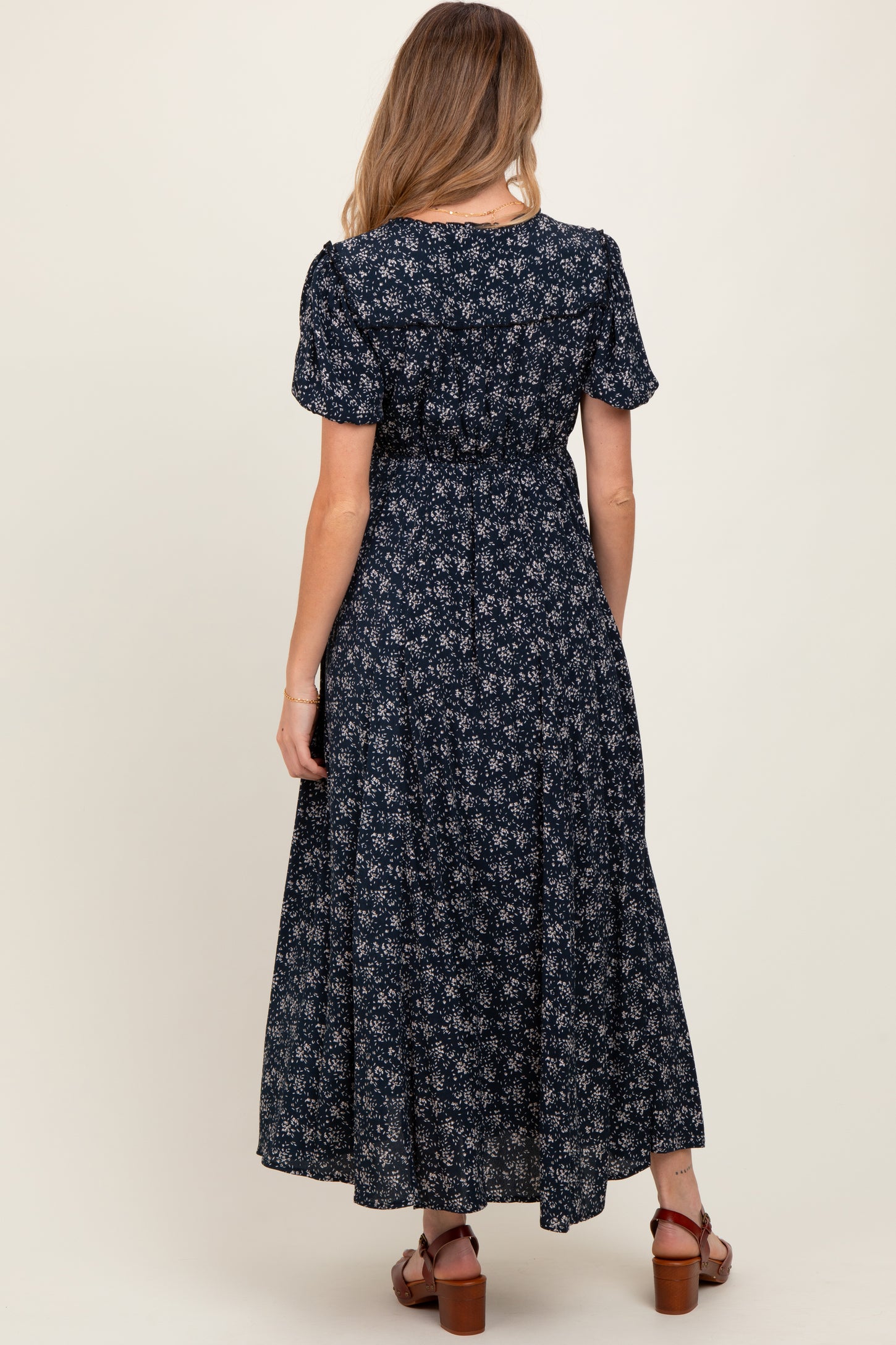 woman wearing a navy floral maternity maxi dress, showing a fitted bodice and flowing skirt from the back