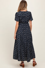 woman wearing a navy floral maternity maxi dress, showing a fitted bodice and flowing skirt from the back