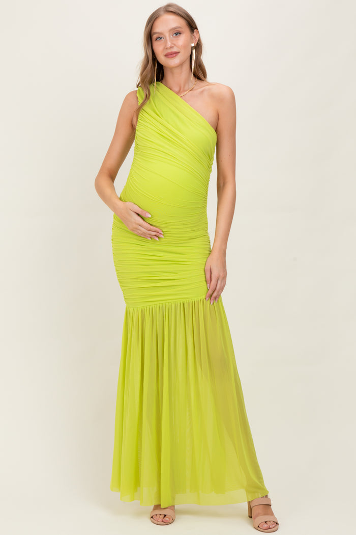 woman wearing a bright neon green one-shoulder maternity gown with ruched detailing and a flowing skirt, showing her baby bump