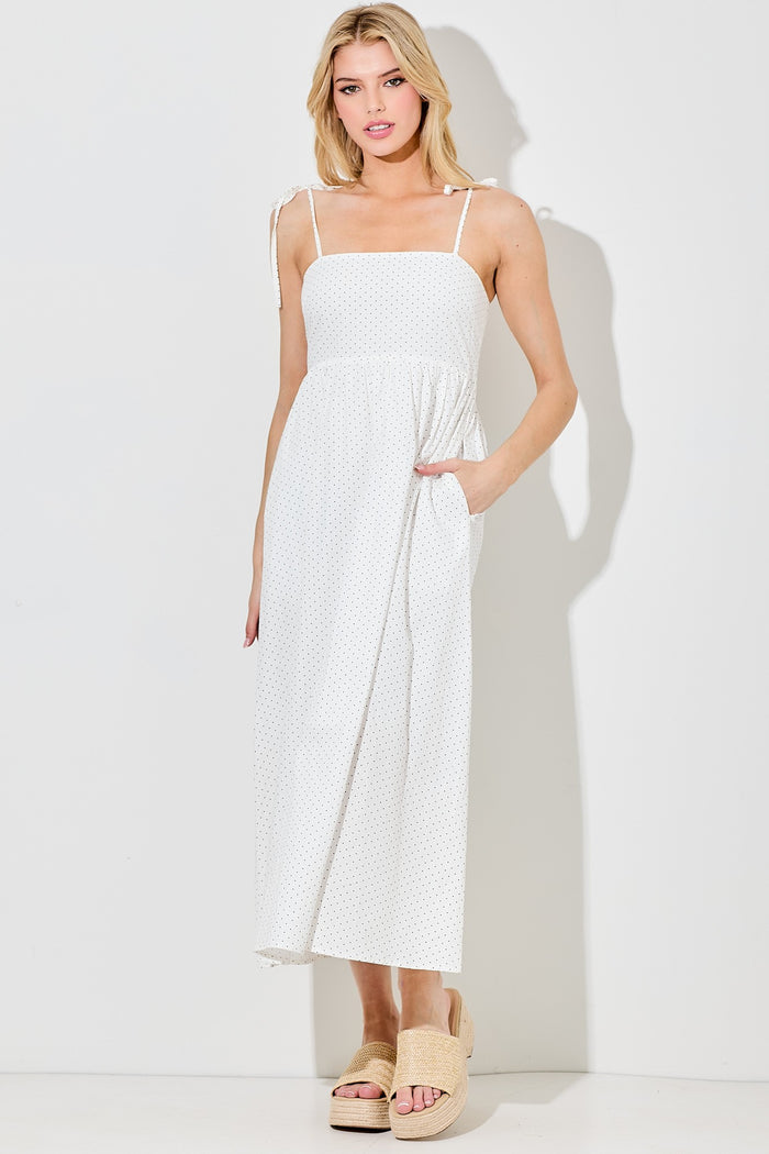 woman wearing a white polka dot maxi dress with adjustable straps and pockets, styled with beige slide sandals