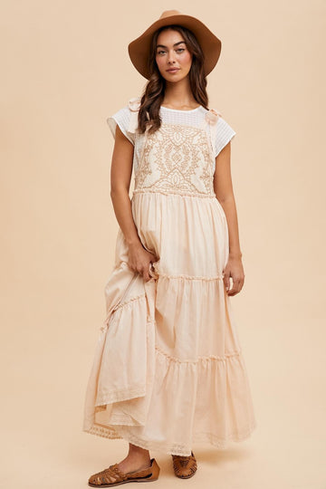 woman wearing a light peach maxi dress with crochet details and a white top, holding the dress and wearing a wide-brimmed hat