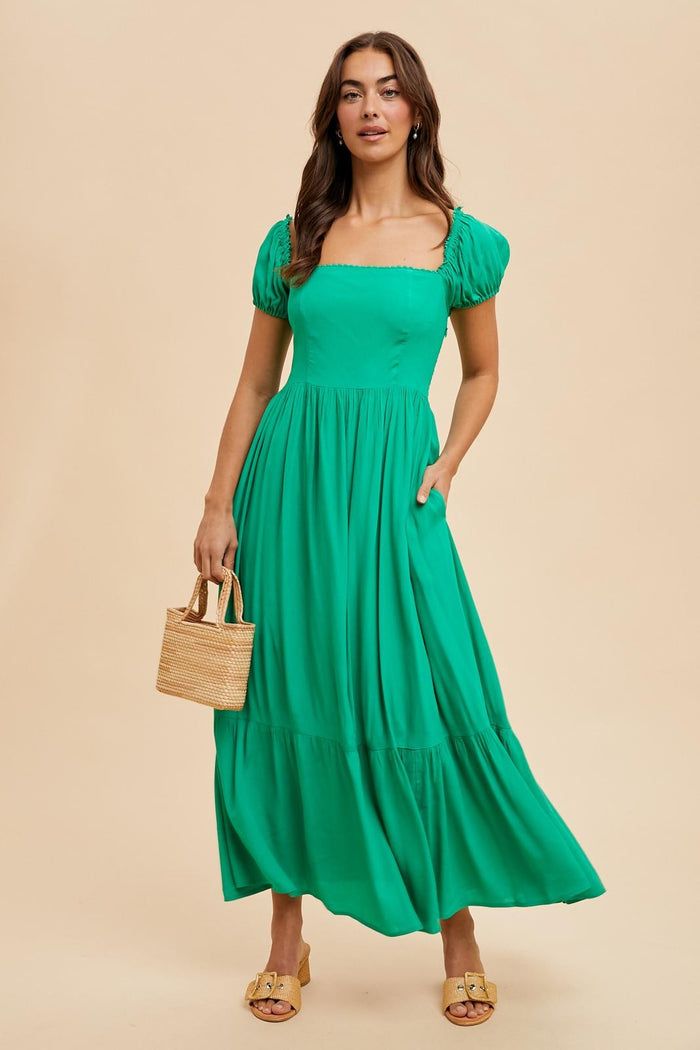 woman wearing a vibrant green maxi dress with puff sleeves and pockets, holding a straw bag