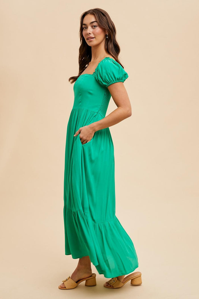 woman wearing a bright green maxi dress with puff sleeves and side pockets, standing against a neutral background
