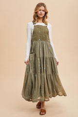 woman wearing a long olive green tiered maxi dress with embroidered flowers and adjustable straps