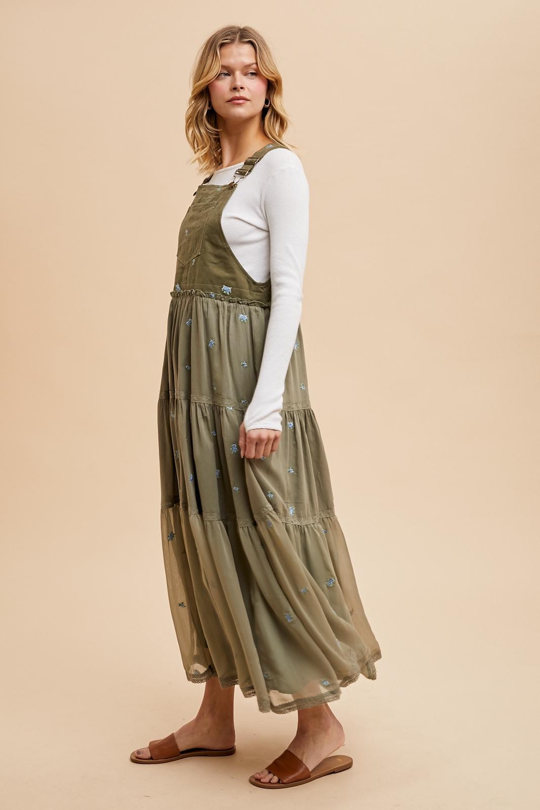 woman wearing an olive green tiered maxi dress with embroidered flowers over a white long sleeve top and sandals